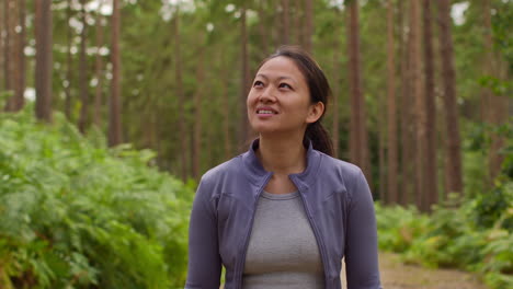 Woman-Wearing-Sports-Clothing-Exercising-Looking-Around-Walking-Along-Track-In-Forest-Enjoying-Peace-And-Beauty-Of-Nature